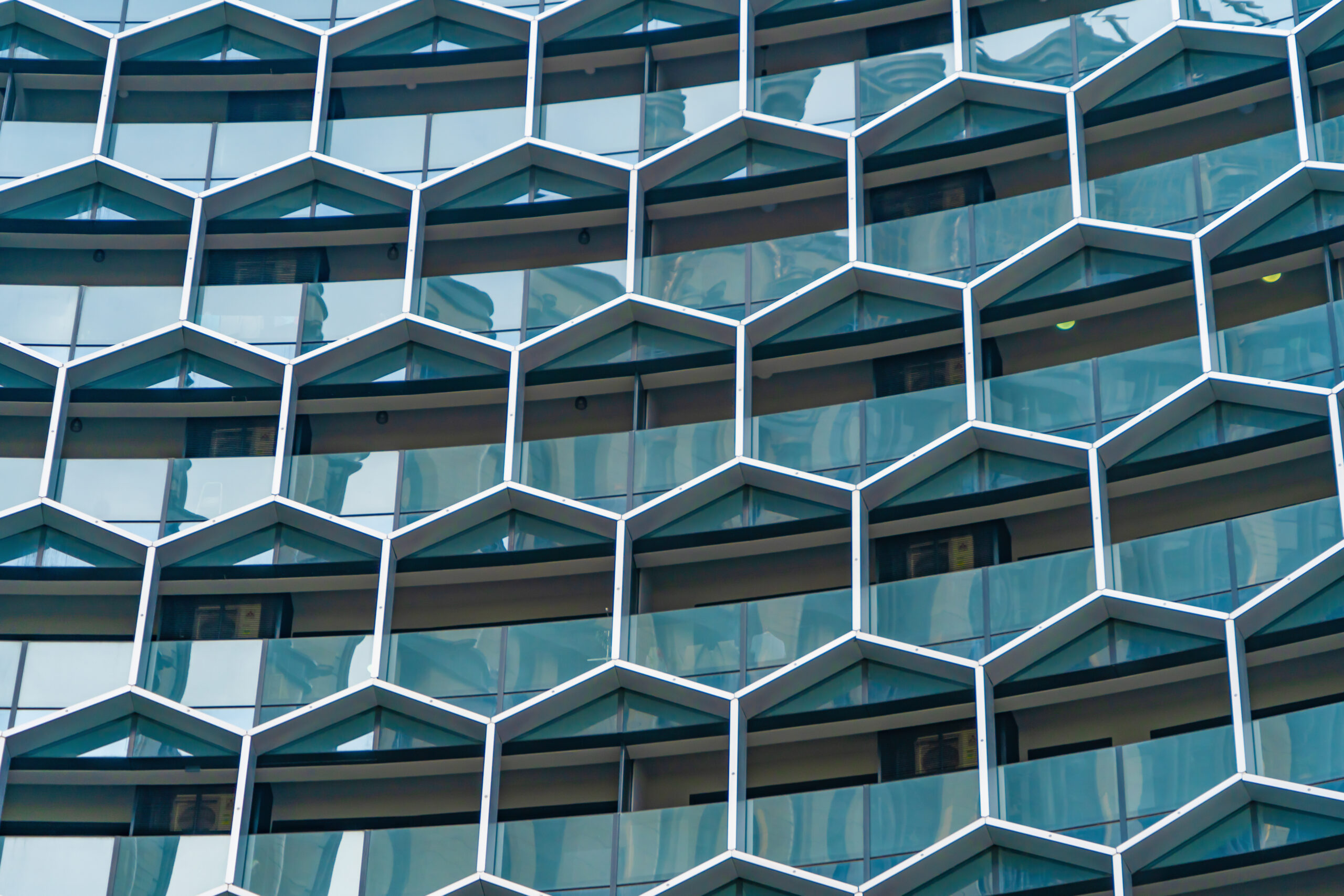 Sicherheitsglas nach Maß kaufen. Moderne Gebäude-Fassade mit hexagonalen Glasfenstern und reflektierender Architektur.